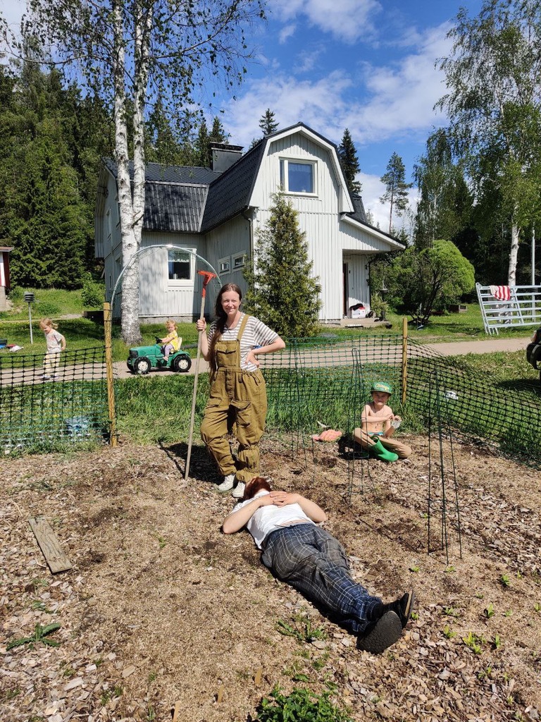 Perhe kasvimaalla vaalean talon edessä kesäpäivänä